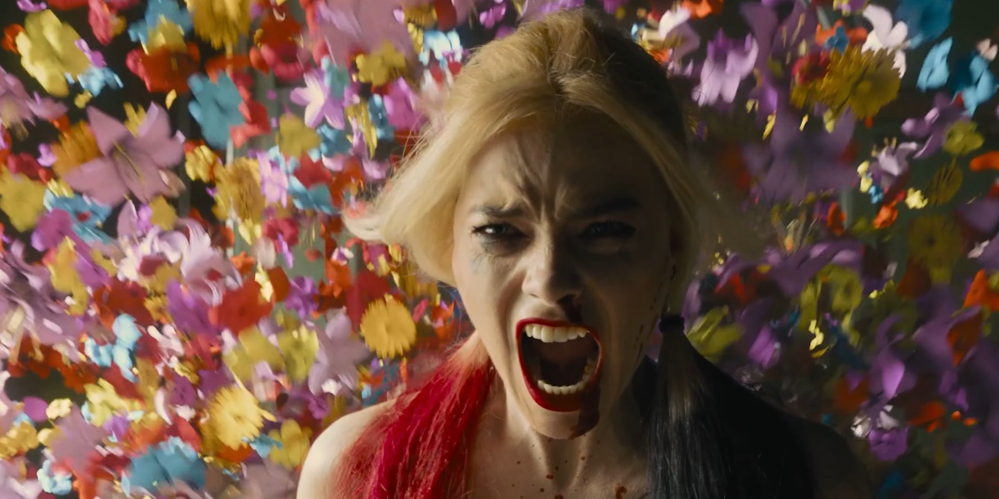 Margot Robbies Harley Quinn letting out a battle cry as flowers shower in The Suicide Squad