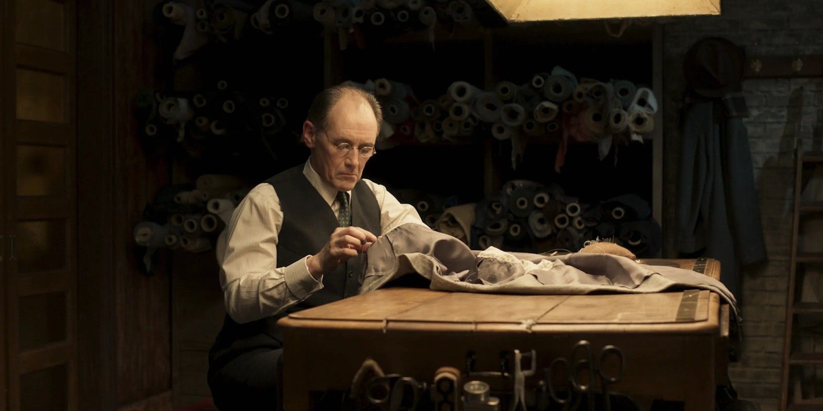 Leonard sewing on his table in The Outfit