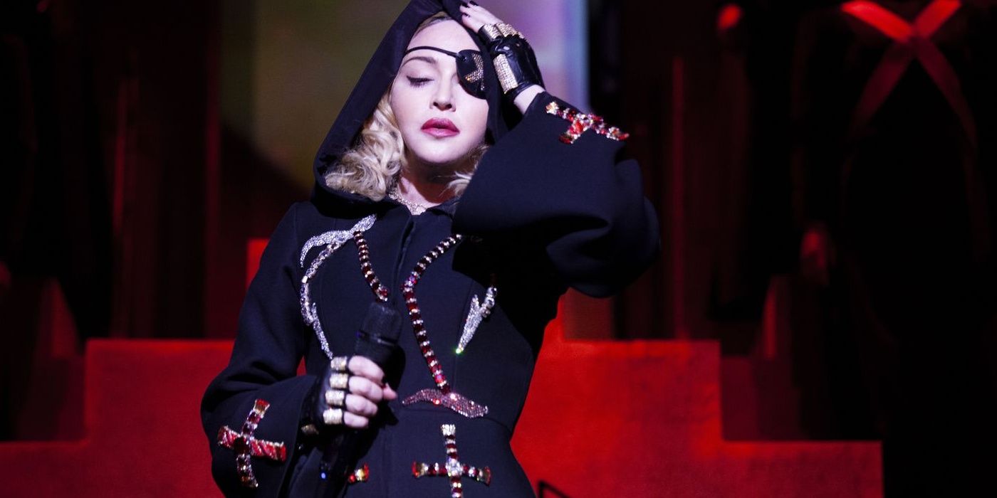 Madonna holding a mic as she holds her head on stage in Madame X Cropped